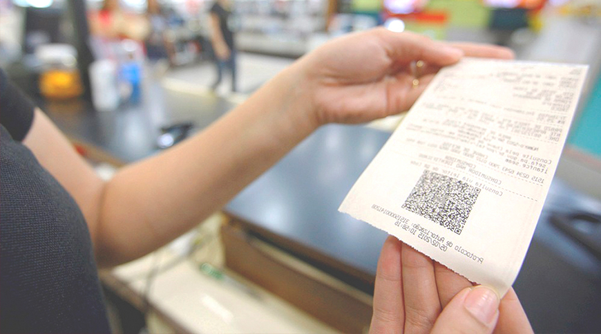 Operadora de caixa segurando o cupom de uma Nota fiscal de consumidor eletrônica com qr-code